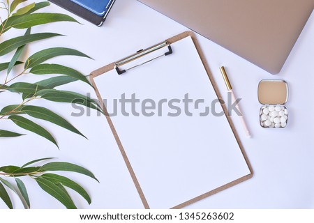 Modern white office desk table with laptop and other supplies. Blank notebook page for input the text in the middle. Top view, flat lay.