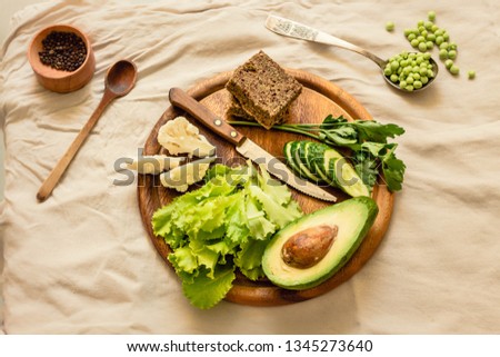 Ingredients for green salad with a piece of bread. Fresh vegetables on a wooden board. Top view.