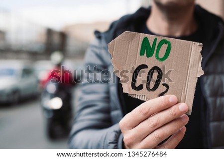 closeup of a young caucasian man, on the street, showing a brown cardboard signboard with the text no CO2 handwritten in it