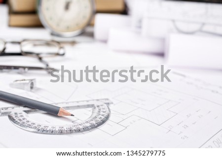 A pencil with a protractor on the background of books, watches and rolls with drawings. Architectural background with rolls of technical drawings and blueprints. selective focus