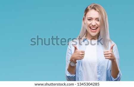 Young blonde woman over isolated background success sign doing positive gesture with hand, thumbs up smiling and happy. Looking at the camera with cheerful expression, winner gesture.