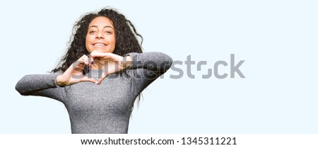 Young beautiful girl with curly hair smiling in love showing heart symbol and shape with hands. Romantic concept.