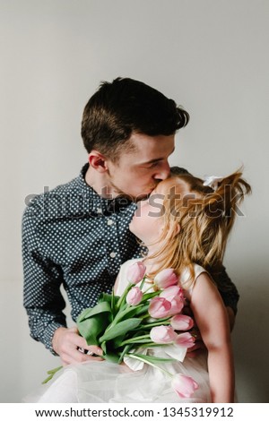 The father holds on his hands little girl on light background indoor. Portrait of dad with flowers and daughter. The concept of family holiday. Father's day. upper half. Close up.