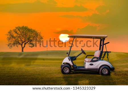 A Golf cart parking on green grass at golf course with big tree and sun set sky background 