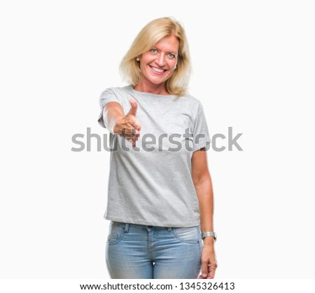 Middle age blonde woman over isolated background smiling friendly offering handshake as greeting and welcoming. Successful business.