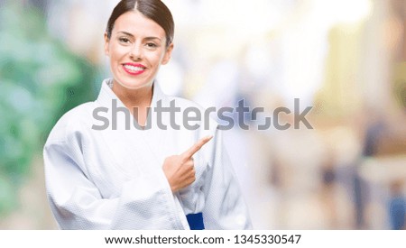 Young beautiful woman wearing karate kimono uniform over isolated background cheerful with a smile of face pointing with hand and finger up to the side with happy and natural expression on face
