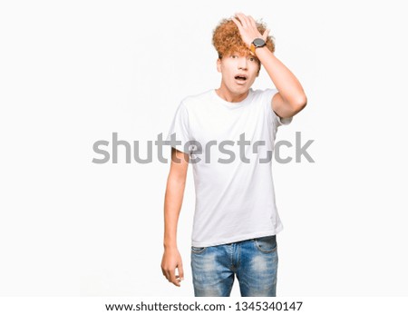 Young handsome man with afro hair wearing casual white t-shirt surprised with hand on head for mistake, remember error. Forgot, bad memory concept.