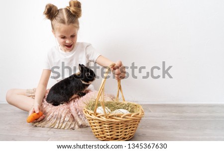 Easter holiday: A girl is holding a little black rabbit and a basket with white eggs.