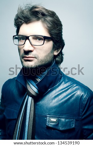 Portrait of a fashionable handsome man in blue jacket with striped scarf over light blue background. Copy-space. Studio shot