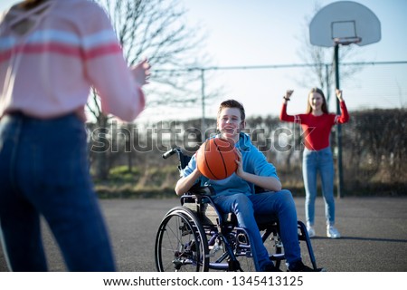 Teenage Boy In Wheelchair Playing Basketball With Friends Royalty-Free Stock Photo #1345413125