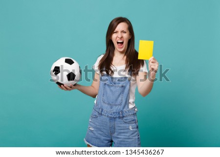 Screaming young woman football fan support team with soccer ball, yellow card, propose player retire from field isolated on blue turquoise background. People emotions, sport family leisure concept