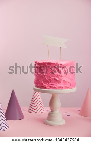 tasty and sweet birthday cake with blank card near party caps on pink 