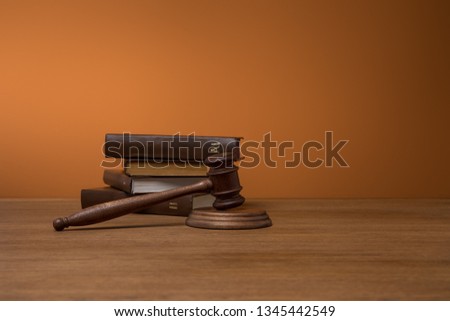 volumes of brown books in leather covers and gavel on wooden table on dark orange background