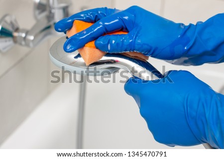 Close-up of the shower faucet and shower head cleaning process from lime scale, white chalk sediment and stains using a commercial soap scum remover. Bathroom cleaning and disinfection, cleanup Royalty-Free Stock Photo #1345470791