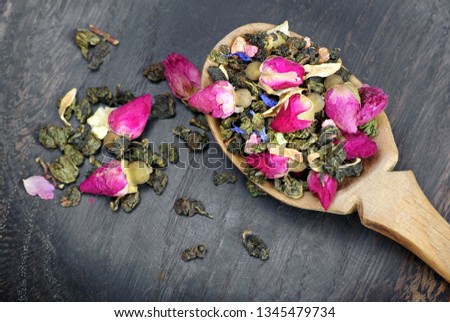 green tea with flowers in a wooden spoon on a dark wooden table. green tea with flowers and dry fruit pieces. blend tea. top view.