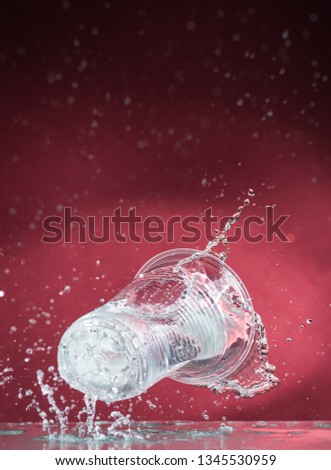 falling one-time transparent glass with clear water and spill water on a red background