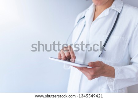 Woman doctor using tablet computer while standing straight in hospital. Doctor with digital tablet. Attractive young female doctor in white lab coat working on digital tablet