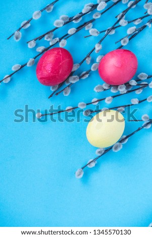 Easter blue background with tricolor boiled Easter eggs (yellow, red) and willow, red ribbon. View from above. Vertical banner