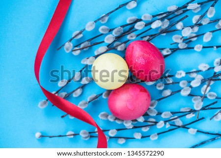 Easter blue background with colorful boiled Easter eggs (yellow, red)) and a willow in the form of a frame, red ribbon. View from above.