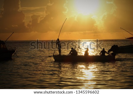 Silhouette of fishermen standing and sitting on a small boat with sunset in the background in Mauritius