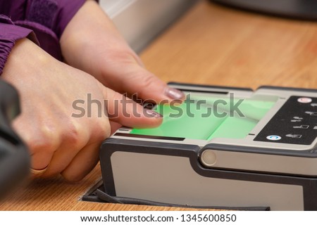 The process of scanning fingerprints during the check at border crossing. Female hand puts fingers to the fingerprint scanner. Identity verification and border control, immigration concept Royalty-Free Stock Photo #1345600850