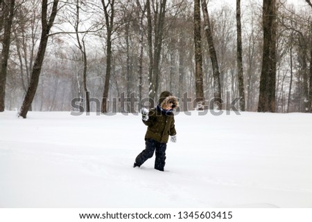 A boy in warm winter clothes Running with a snowball in his hand for playing snowballs, blizzard, a large amount of snow falls, the territory of the city park