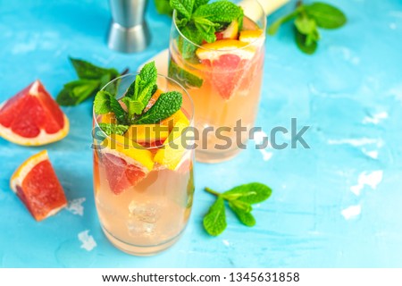 Grapefruit and fresh mint cocktail with juice, cold summer citrus refreshing drink gin tonic cocktail or beverage with ice on blue concrete surface.