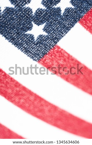 An extreme macro or close-up shot of a small American flag's blue stars and red stripes printed on a rough fabric in vertical image format.