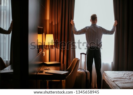 Businessman working from hotel. Guy opening the curtains at the hotel room.