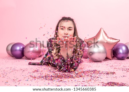 Funny girl blows confetti in her hands. Color Balloons on a pink background. The concept of the party and holiday