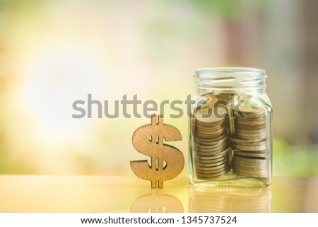 Dollar sign icon and pile of coins in glass jar or piggy bank on wooden table on blurred background with copy space. Business, financial, savings, investment concept