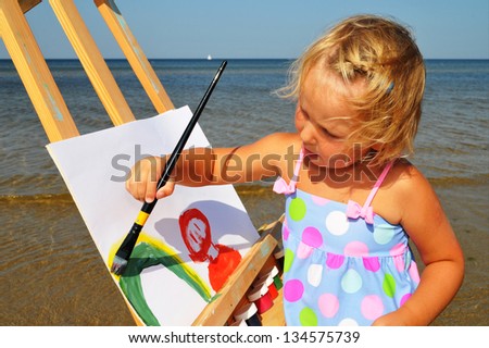 Cute little girl paints on the beach