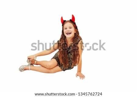 A little girl with devil horns in an evening dress with shoes and makeup sits and emotionally expressing emotions, isolated on a white background