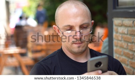 Late 20s Caucasian Man Texting on Smartphone in Outdoor Cafe