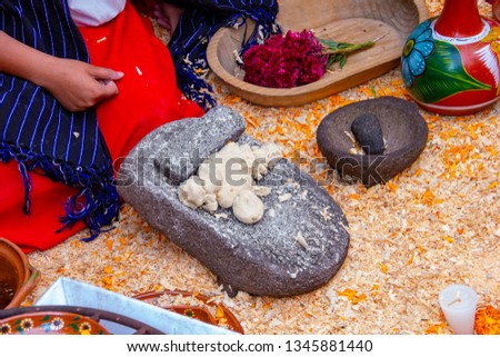 close up a woman kneeling on a bed of cempasuchil petals kneading corn grains on a stone molcajete