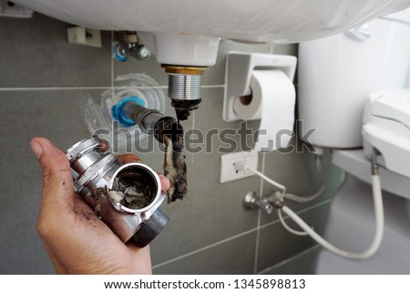 Hand of Plumber holding joints and connections of Basin or sink in a bathroom, Clearing a Clogged Bathroom Sink in a bathroom for unclog a Sink.	                                Royalty-Free Stock Photo #1345898813