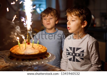 Two beautiful kids, little preschool boys celebrating birthday and blowing candles on homemade baked cake, indoor. Birthday party for siblings children. Happy twins about gifts and fireworks on tarte
