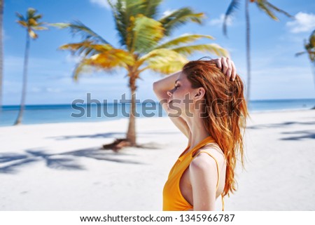 A woman in a yellow swimsuit cropped view of the sea vacation ocean yellow sand green trees palm trees the sun                       
