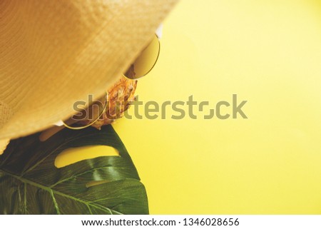 Fresh ripe pineapple with sunglasses in hat and a leaf of monstera tree on color background, top view.