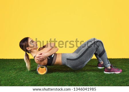 Photo amazing fit young woman do exercise with foam roller on green grass over yellow background.