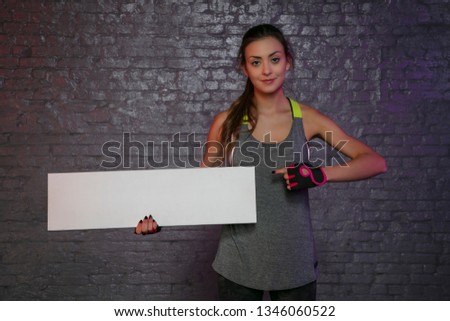 beautiful young girl holding an empty board, copy space for advertising, muscles and gym, conceptual photo, advertising space