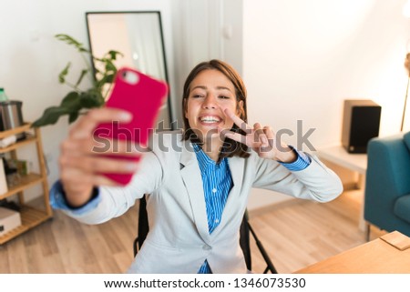 Young beautiful happy successful business woman taking selfies with her phone. Having fun at work.