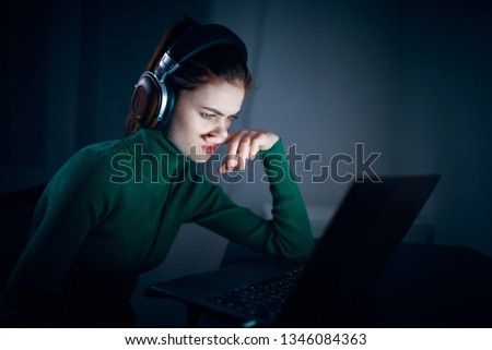 Woman in headphones in front of a laptop at night sits and works