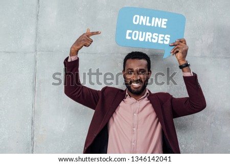 smiling african american casual businessman looking at camera and pointing with finger at speech bubble with online courses lettering