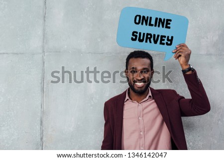 smiling african american casual businessman looking at camera and holding speech bubble with online survey lettering