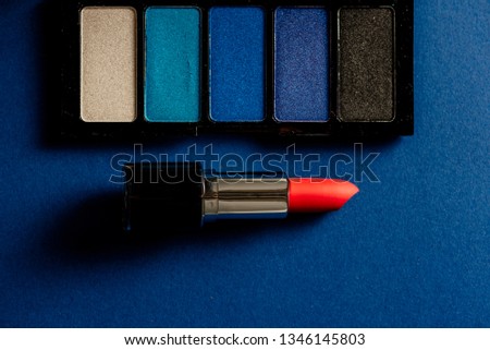 Pink lipstick and blue eyeshadow palette and blue background. Product concept