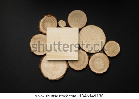Pine tree cross-sections with annual rings and wooden square on black background. Lumber piece close-up shot, top view.