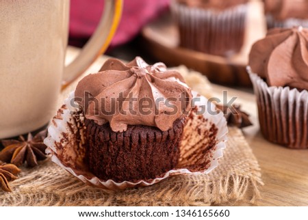 Closeup of a chocolate cupcake with creamy icing and cupcakes and coffee cup in background