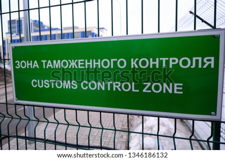 Customs control zone - a sign in Russian and English at the entrance to the vehicle inspection point. The plate is green on the metal grill. Pointer and warning about entering a special area.