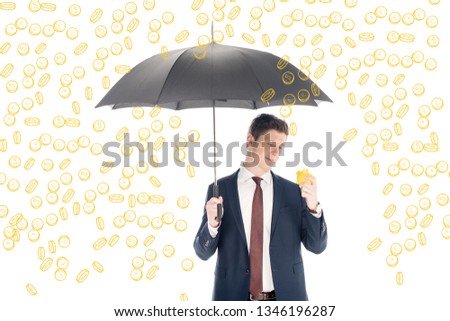 successful businessman in suit holding umbrella and yellow piggy bank under coins rain on white background